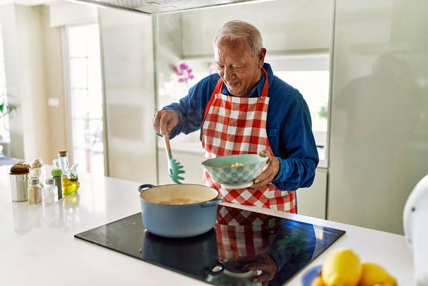 Старший чоловік посміхається впевнено готує спагеті на кухні
 - Фото, зображення