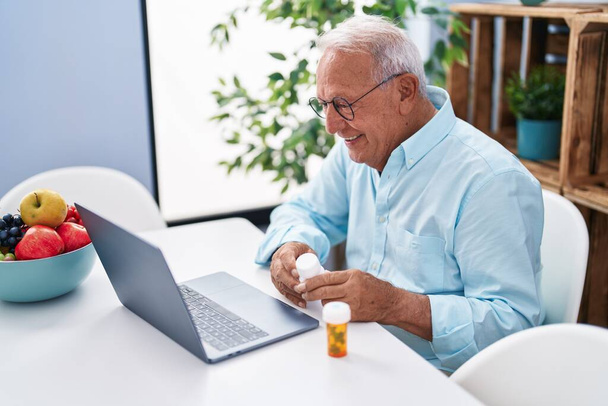 Senior grey-haired man having telemedicine sitting on table at home - Photo, image