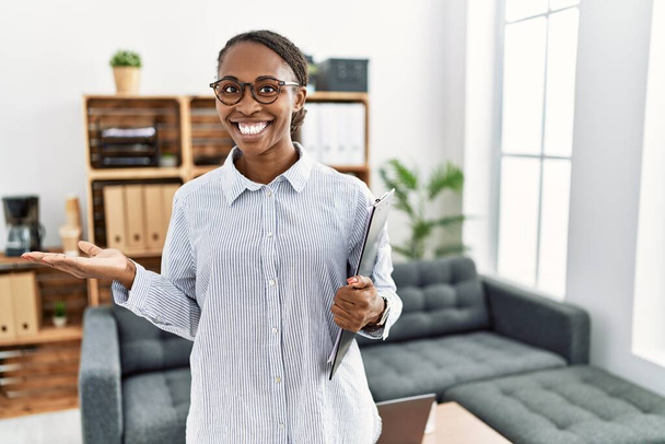 African woman working at psychology clinic pointing aside with hands open palms showing copy space, presenting advertisement smiling excited happy  - Zdjęcie, obraz