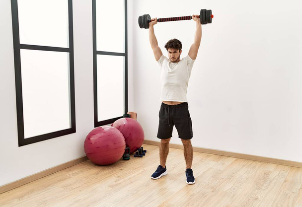 Young hispanic man training with dumbbell at sport center - Photo, Image