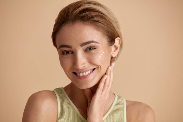 Skin Care Woman Posing with Cream on Cheek. Closeup Of Beautiful Smiling Girl with Moisturizer On Fresh Soft Pure Skin. Portrait Of Woman With Natural Makeup Recommended Beauty Cosmetics Product  - Fotografie, Obrázek