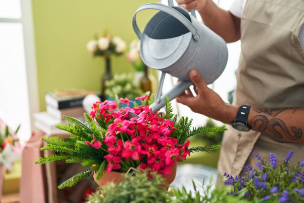 Young latin man florist watering plant at flower shop - Foto, imagen