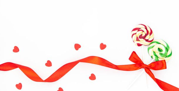 Dois belos pirulitos amarrados com uma fita vermelha em um arco e corações decorativos em um fundo branco isolado, espaço de cópia. - Foto, Imagem