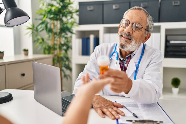Starszy siwowłosy lekarz uśmiechający się pewnie przepisują pigułki w klinice - Zdjęcie, obraz