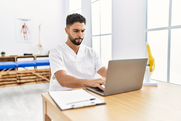 Young arab man wearing physiotherapist uniform using laptop at clinic - Photo, Image