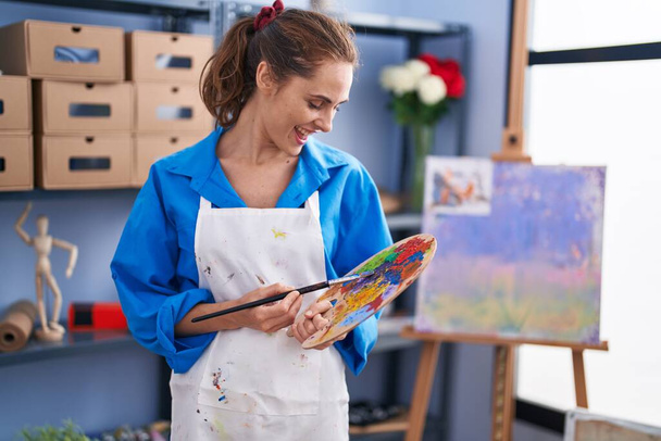 Young woman artist holding paintbrush and palette at art studio - Фото, изображение