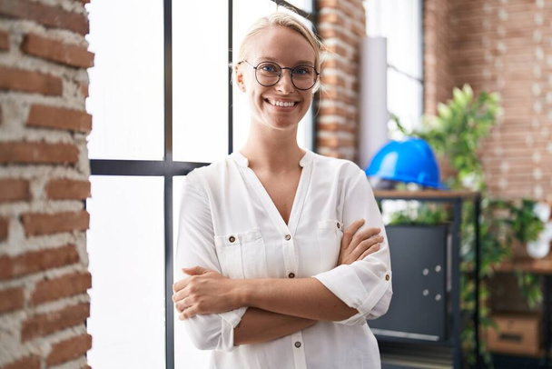 Young blonde woman business worker standing with arms crossed gesture at office - Foto, afbeelding