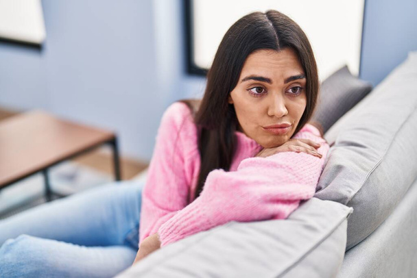 Young hispanic woman with boring expression sitting on sofa at home - Foto, Bild