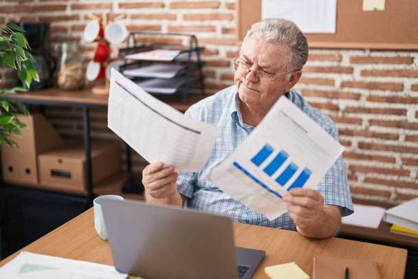Średni wiek siwowłosy mężczyzna pracownik biznesu za pomocą laptopa czytania dokumentu w biurze - Zdjęcie, obraz