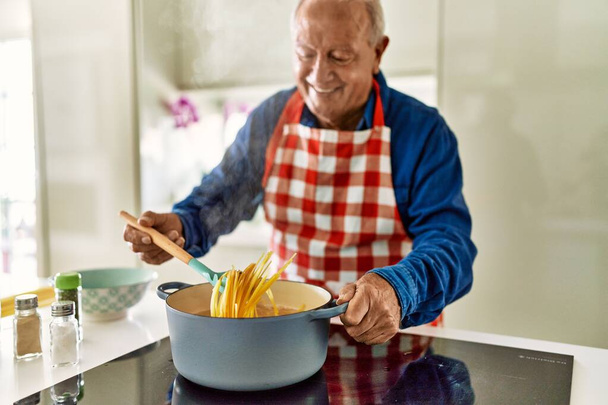 Старший чоловік посміхається впевнено готує спагеті на кухні
 - Фото, зображення