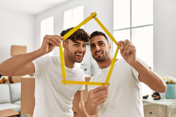 Two hispanic men couple smiling confident holding house project at new home - Photo, Image