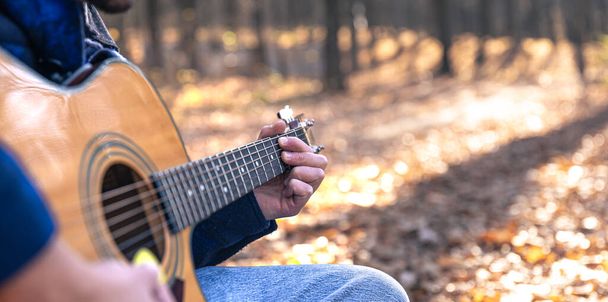 Close-up, a man plays an acoustic guitar in the forest during the cold season, copy space. - Photo, Image