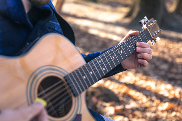 Primer plano, un hombre toca una guitarra acústica en el bosque durante la estación fría. - Foto, Imagen
