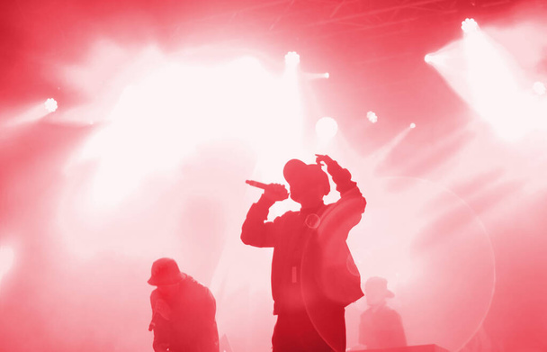Silhouette della band rap che si esibisce sul palco in luci rosse brillanti. Irriconoscibile giovane rapper che canta in concerto - Foto, immagini