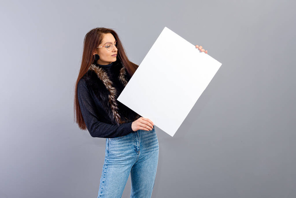 Zarif genç bir bayan, gri üzerinde izole edilmiş, fotokopi alanı ile boş tabela gösteriyor. - Fotoğraf, Görsel