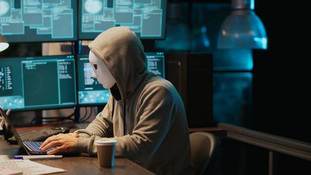マスクハッキングデータベースサーバーを持つサイバーテロリスト、コンピュータシステムをハッキングし、マルウェアを作成するためにウイルスを活性化させるフード付きハッカー。ビッグデータを盗み情報を漏洩. - 写真・画像