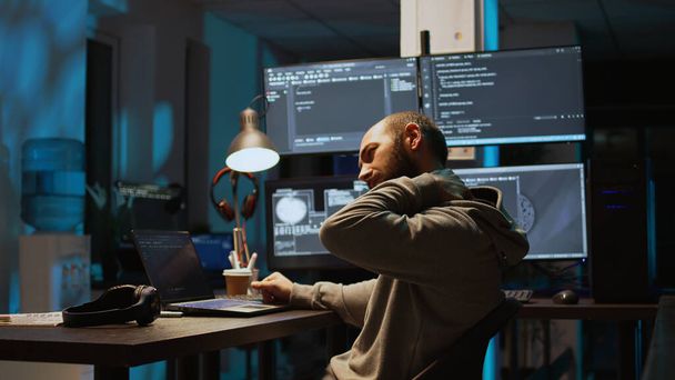 Mężczyzna programista internetowy pisze kod i radzi sobie z bólem pleców, siedzi w biurze i czuje dyskomfort kręgosłupa w nocy. Programista aplikacji kodujący skrypt html w oknie terminala. Strzał ręczny. - Zdjęcie, obraz