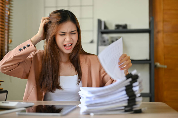Wütend und verrückt schreit eine asiatische Geschäftsfrau oder Buchhalterin, die mit der Arbeit ihres Assistenten unzufrieden ist, während sie sich die Papiere des Berichts ansieht.. - Foto, Bild