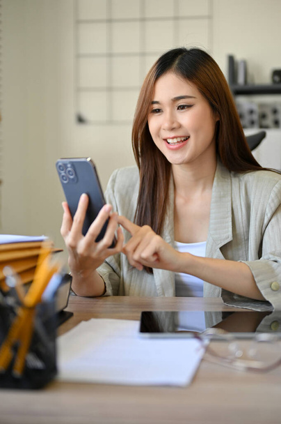 Portrait, elegante asiatische Geschäftsfrau im Millennium oder Büroangestellte am Schreibtisch, die mit ihrem Smartphone mit Freunden chatten, online einkaufen und E-Mails verschicken. - Foto, Bild