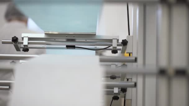 Close-up van witte en blauwe katoenen vezels die samensmelten tot medische gezichtsmaskers in een fabriek. Geautomatiseerde machines voor het vervaardigen van medische maskers voor de ademhaling.  - Video