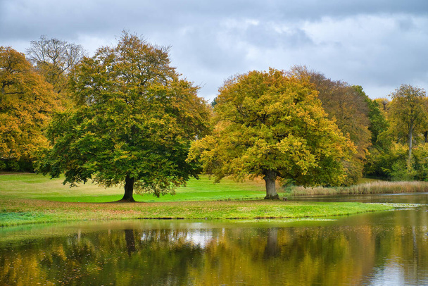 Frederiksborg Castle Park in de herfst met machtige loofbomen worden ze weerspiegeld in het gecreëerde meer. Heldere kleuren van de bladeren. Wandeling in Denemarken - Foto, afbeelding