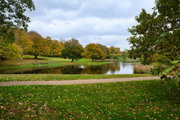 Schlosspark Frederiksborg im Herbst mit mächtigen Laubbäumen auf den Gartenwiesen und dem angelegten See. Bunte Farben der Blätter. Spaziergang in Dänemark - Foto, Bild