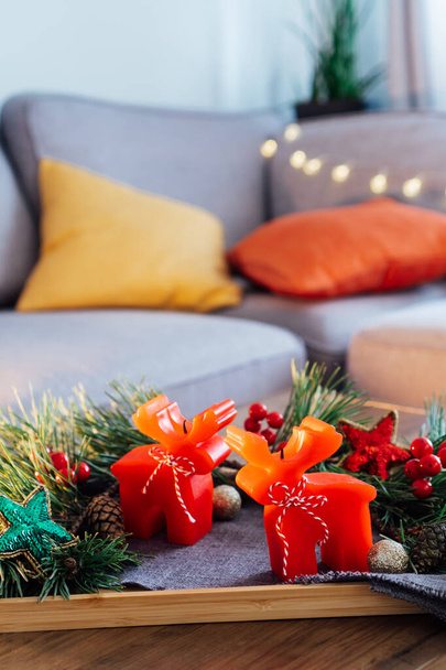 Christmas cozy mood composition for hygge home decor. Deer shape red candles, fresh green pine branches and festive Xmas decor on tray on the coffee table in living room. Vertical. Selective focus - Foto, Imagen
