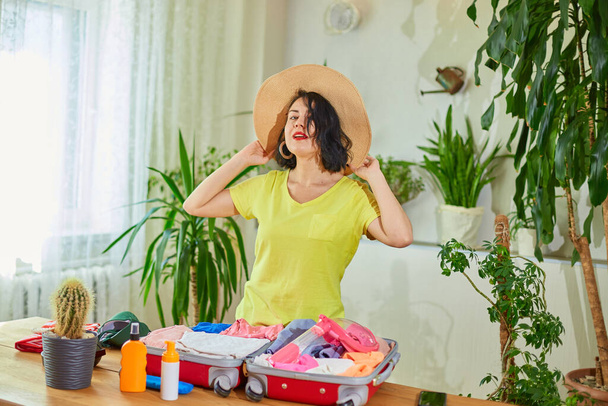 Mulher feliz no chapéu dançando, mala de embalagem, preparando-se para a viagem de férias de verão preparando a bagagem para viagens de férias. - Foto, Imagem