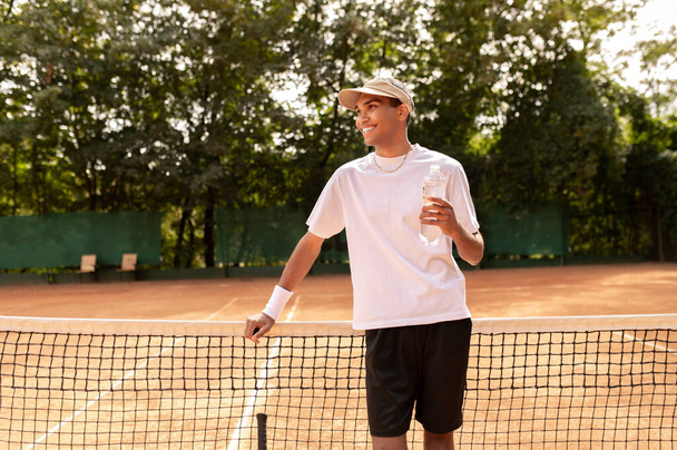 Tennis player. Young man in white thsirt standing at the tennis court - Fotó, kép
