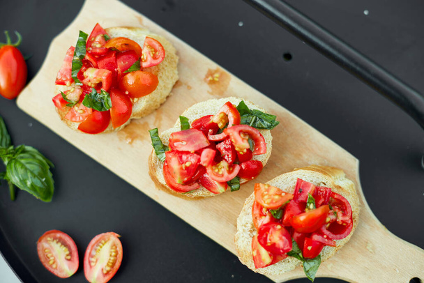 Italian bruschetta with fresh red tomatoes and basil herbs on a wooden board outdoor on the yard, backyard at home, sunlight. Classic Italy food, antipasto - Photo, Image