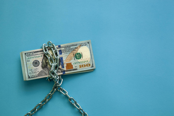 Hundred dollar bills wrapped in a chain on a blue background. Concept of economy, finance and exchange rate - Foto, Imagen