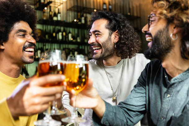 Šťastní mnohonárodnostní přátelé pijící pivo v pivovarském baru. Různí mladí lidé slaví společně roztleskávání s nápoji v irské hospodě - Fotografie, Obrázek