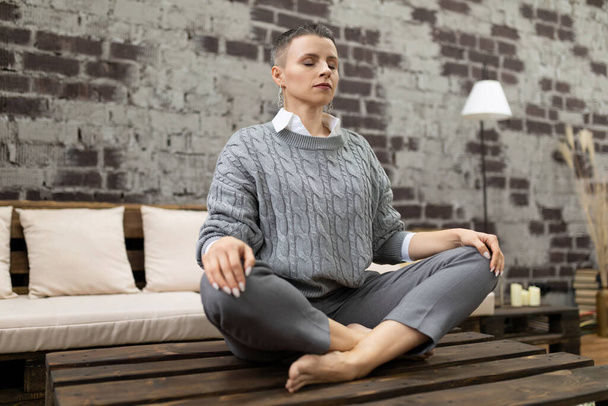 Erwachsene kaukasische Frau meditiert zu Hause sitzend in Yoga-Pose. - Foto, Bild