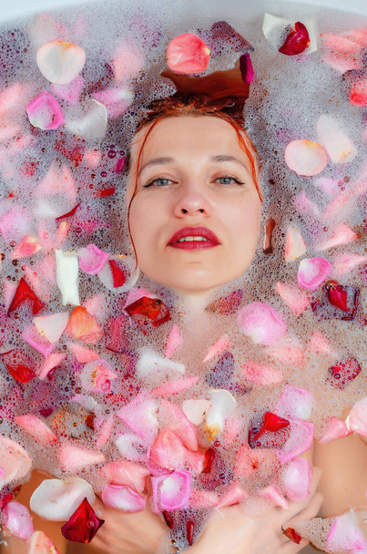 visage d'une belle femme dans la salle de bain parmi les pétales de mousse et de rose - Photo, image