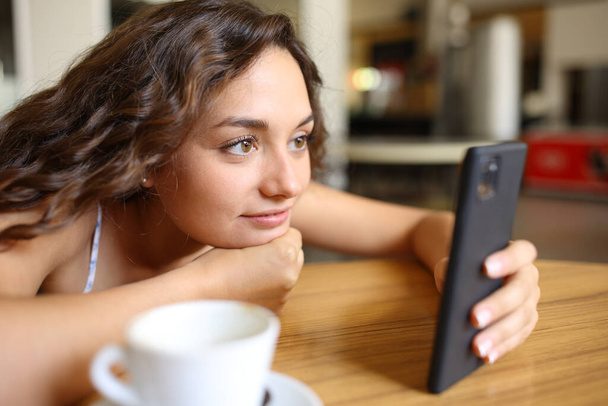 Woman checking smart phone content sitting in a coffee shop - Photo, Image