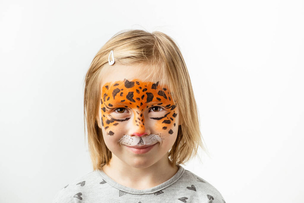Cute little kaukaska dziewczyna z tygrysem malowanie twarzy na białym tle. Zbliż portret małego dziecka z malowaniem twarzy. Rok tygrysa. Szczęśliwa uśmiechnięta dziewczyna - Zdjęcie, obraz