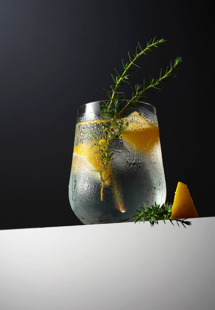 Coquetel Gin-tônico com limão, ramo de zimbro e gelo em um fundo escuro. Espaço de cópia.  - Foto, Imagem