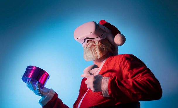 Santa Claus nosić vr kask gadżet urządzenia sprzęt oglądanie realistyczne doświadczenie i trzymać prezent na Boże Narodzenie, doświadcza wirtualnej rzeczywistości - Zdjęcie, obraz