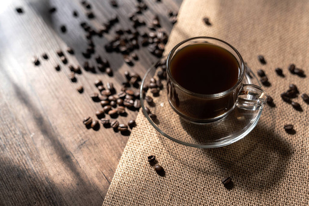 Forró kávé átlátszó kávéscsészében és kávébab öreg fán meleg fényben, fénymásoló hellyel. - Fotó, kép