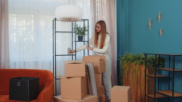 Женщина входит в комнату с картонными коробками, распаковывает пакеты с мебелью интерьера после аренды или покупки нового жилого дома. Девушка сосредоточилась на переезде. Люди образ жизни - Фото, изображение