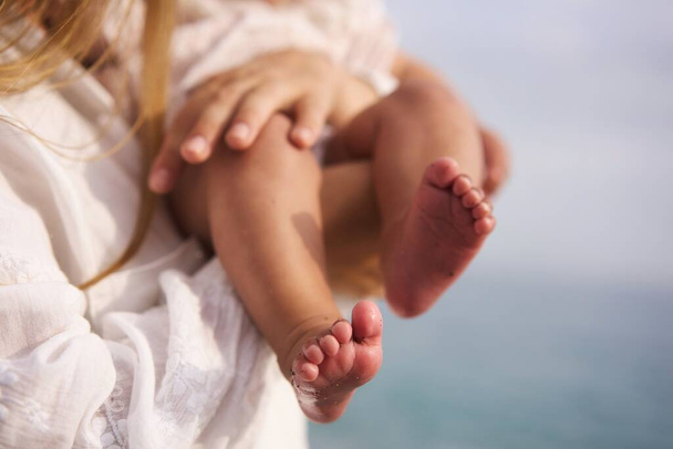 Bare feet of a cute newborn baby in warm white clothes at the sea. Childhood. Small bare feet of a little baby girl or boy. Sleeping newborn child. High quality photo - Φωτογραφία, εικόνα