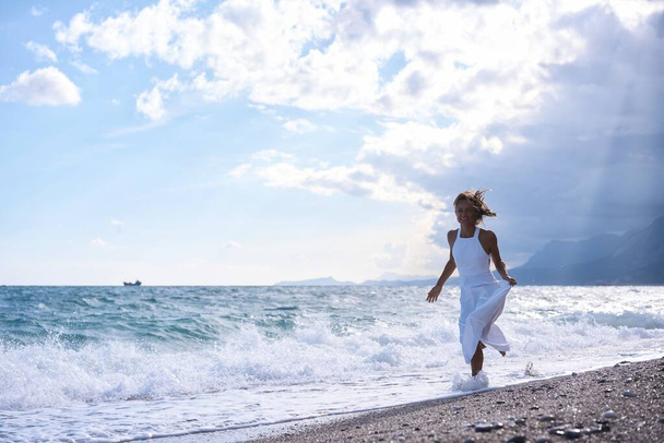Eine Frontansicht eines jungen glücklichen Mädchens, das am Strand läuft. Hochwertiges Foto - Foto, Bild