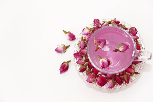 růžový čaj v průhledném skleněném hrnku a malé pupínky suché růžové růže na bílém pozadí - Fotografie, Obrázek