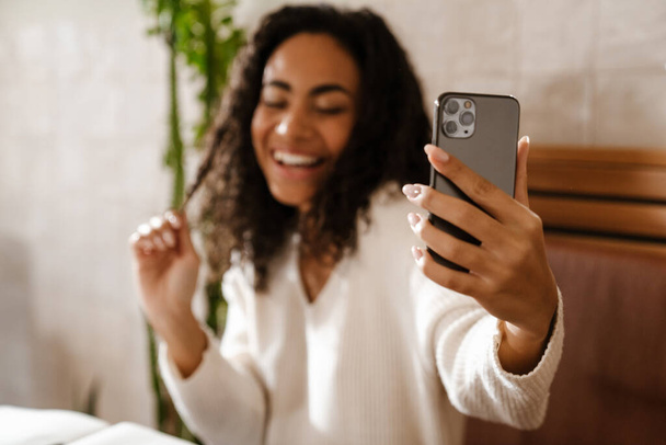 Young black woman laughing and taking selfie photo on cellphone in cafe indoors - Valokuva, kuva