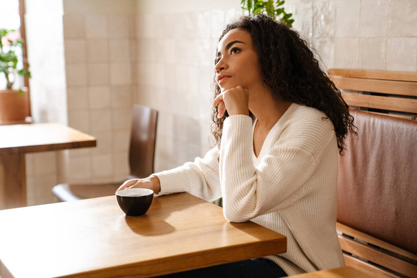 Young black woman drinking coffee while sitting in cafe indoors - Foto, afbeelding