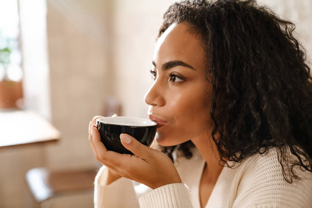 Genç siyah kadın kafede otururken kahve içiyor. - Fotoğraf, Görsel