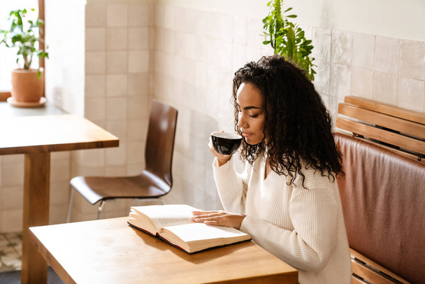 Jovem mulher negra bebendo café e leitura livro no café dentro de casa - Foto, Imagem
