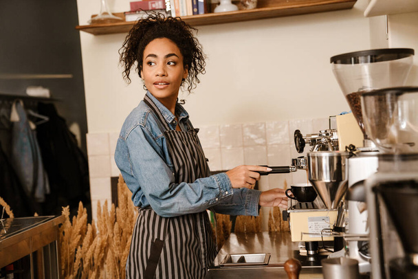 Young black barista wearing apron making coffee while working in cafe indoors - Fotografie, Obrázek
