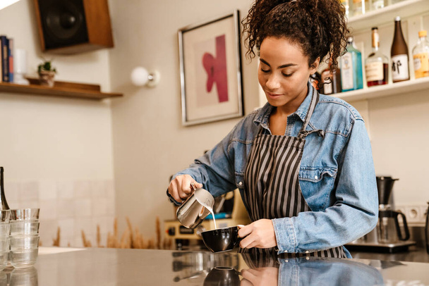 Young black barista wearing apron making coffee while working in cafe indoors - Photo, image
