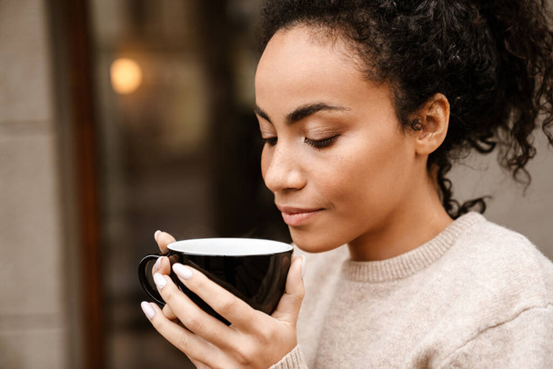 Young black woman smiling and drinking coffee in cafe outdoors - Φωτογραφία, εικόνα